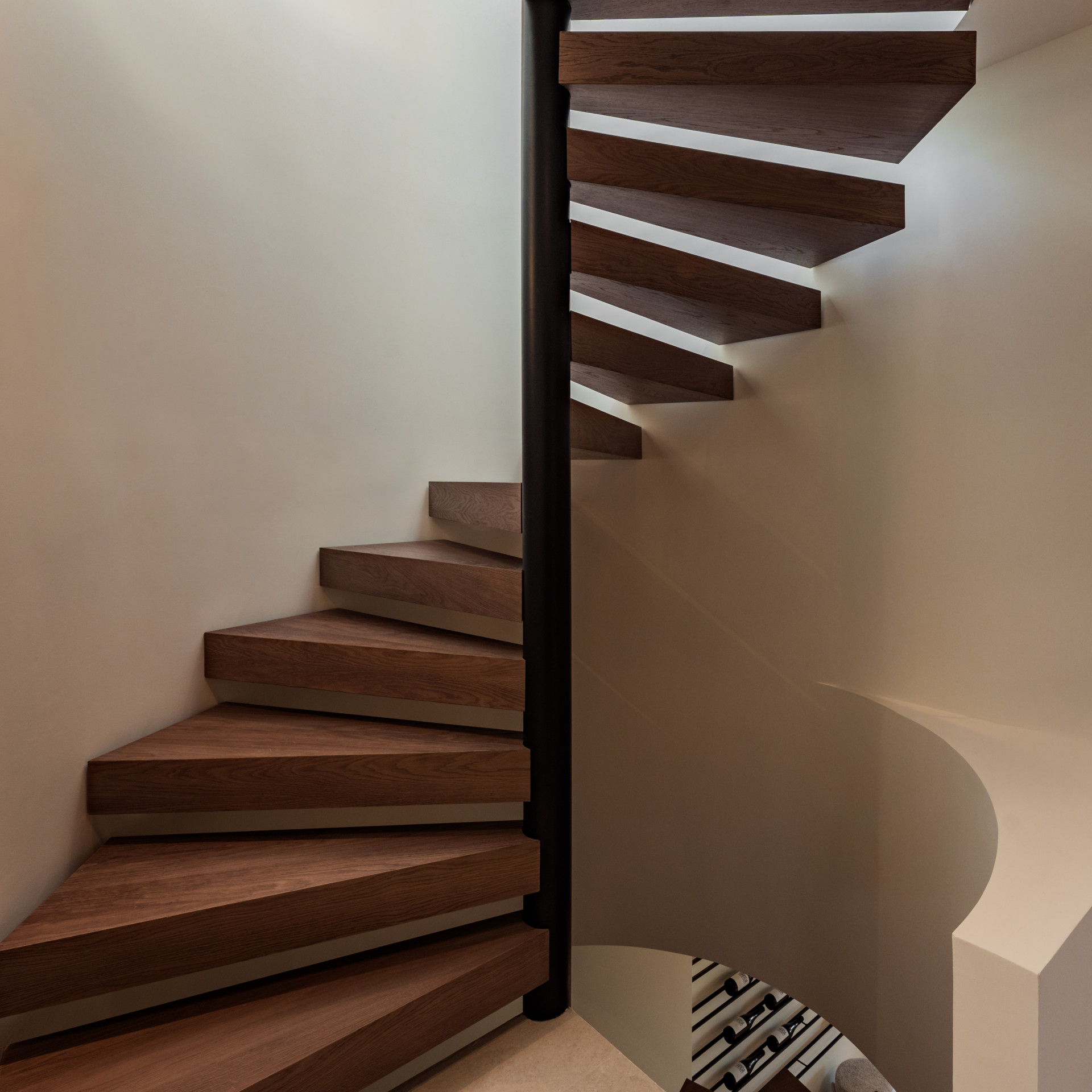 Full height view of a modern spiral staircase with dark wood treads and a black central column.