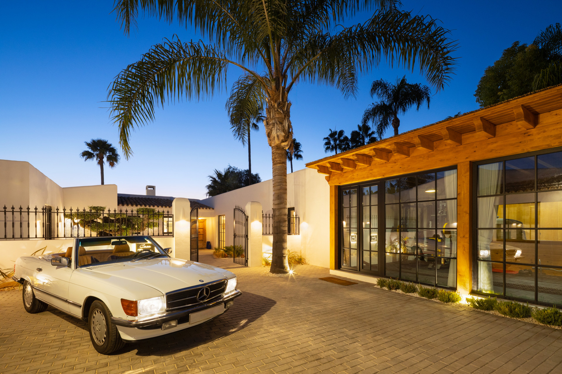 Exterior view of the villa at dusk with a white classic car parked in a paved driveway.