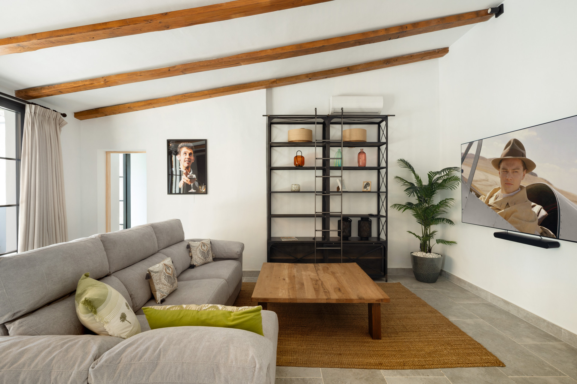 Living room with gray sofa, wooden coffee table, wall-mounted TV, and exposed ceiling beams.