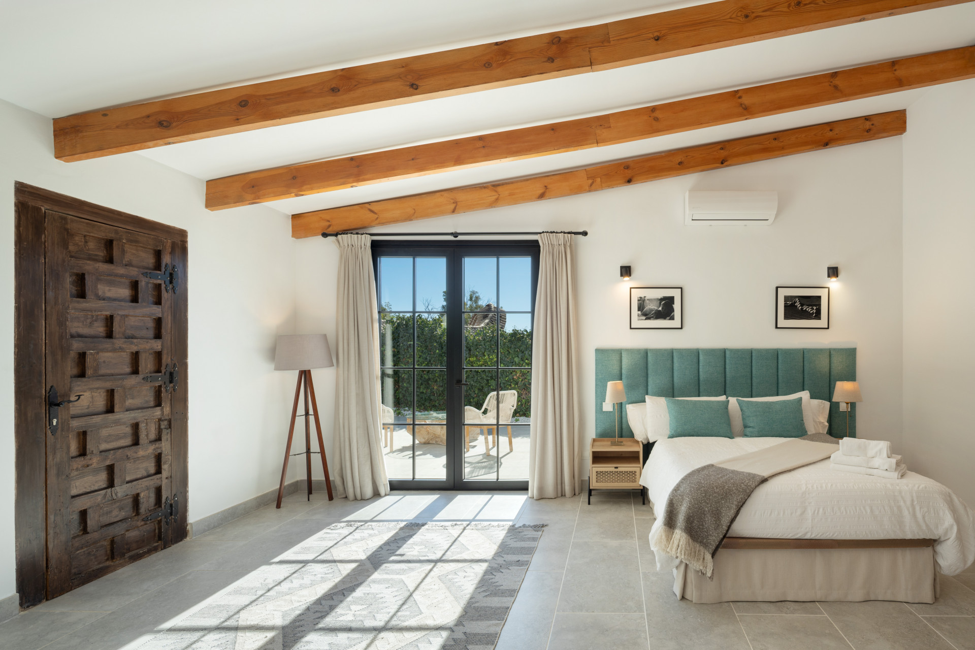 Bedroom with a teal headboard, white bed, dark wood door, and glass doors leading to a patio.