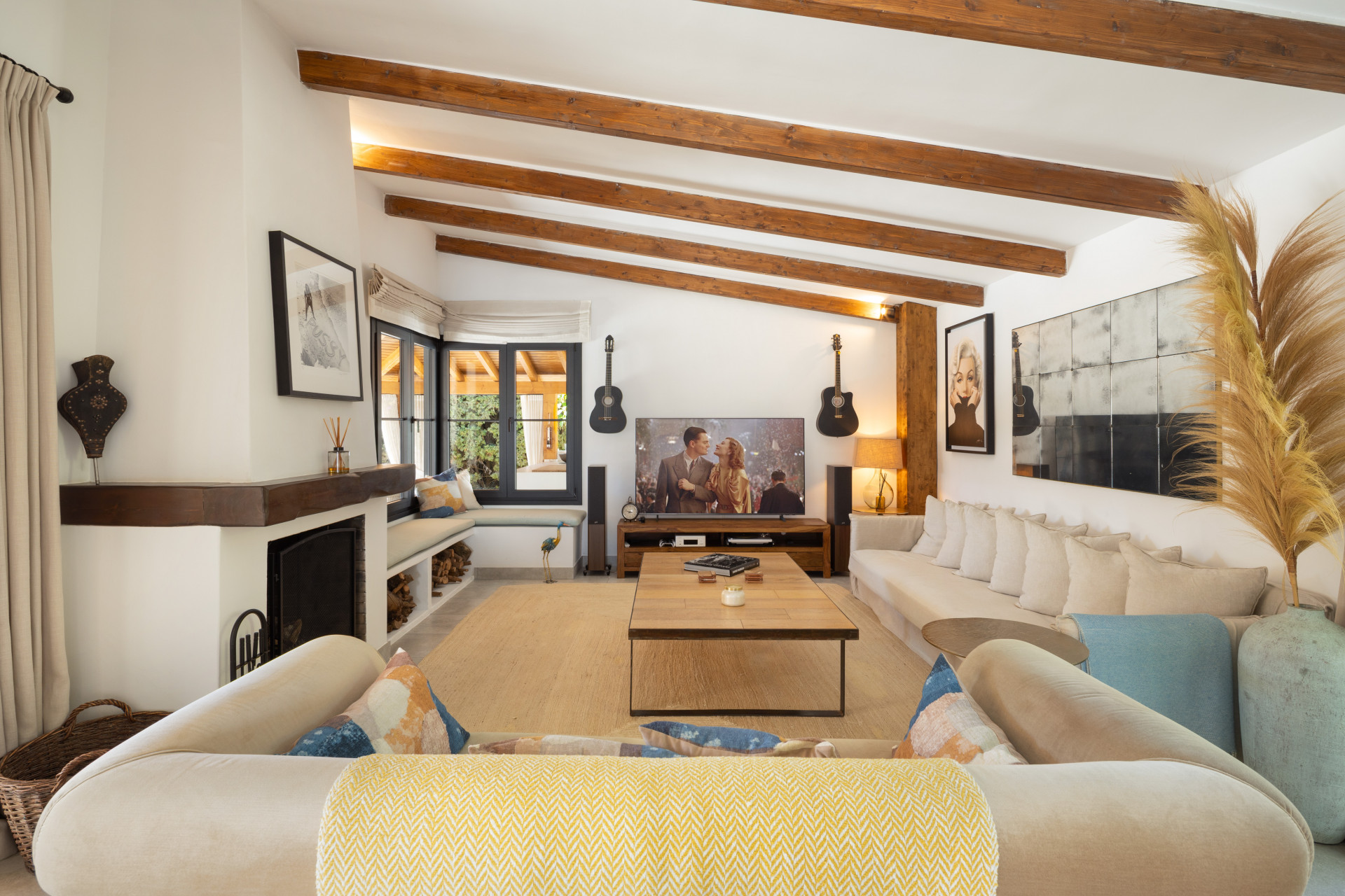 Living room with beamed ceiling, fireplace, two large sofas, coffee table, and a large television.