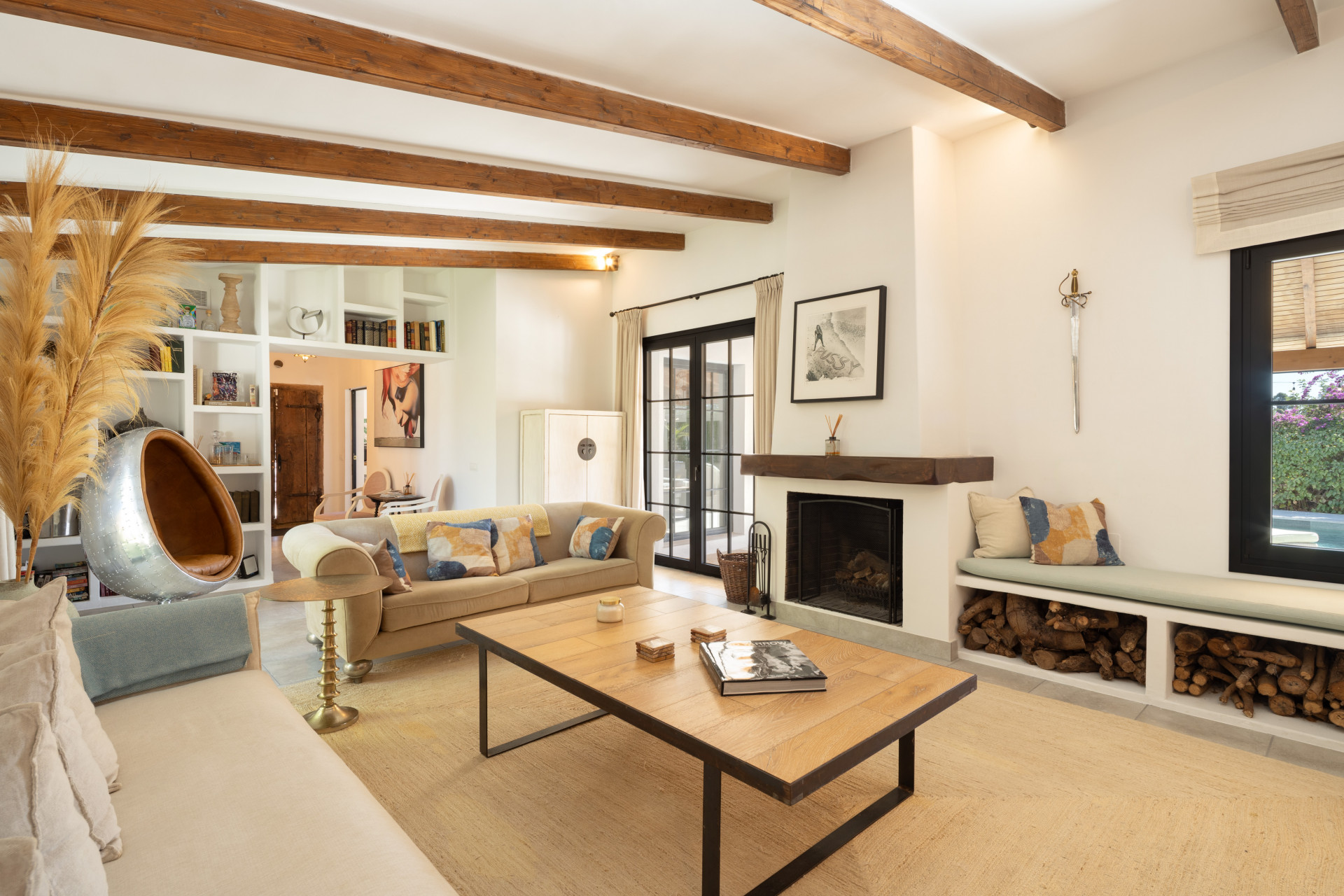 Living room with beige sofas, a wooden coffee table, fireplace, and exposed wooden ceiling beams.
