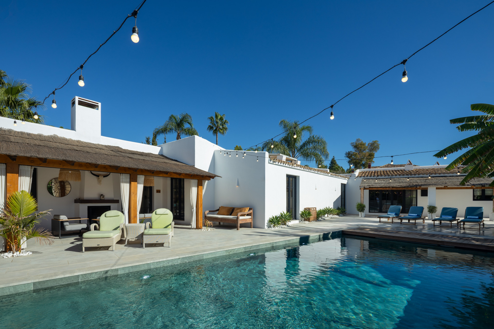 Outdoor area with a large swimming pool, lounge chairs, covered patio, and string lights overhead.