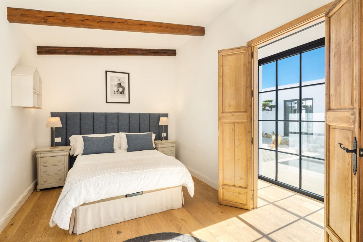 Bedroom with wooden floor and exposed beams, a blue headboard bed, and an open door to an outdoor patio.
