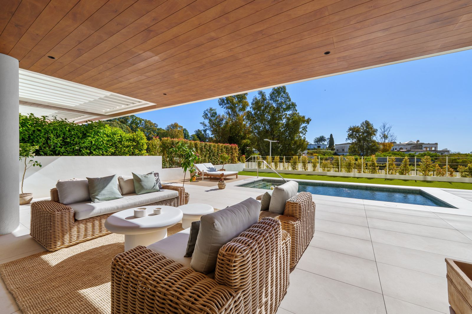 Outdoor patio with wicker furniture, a small pool, and lounge chairs under a wooden ceiling.