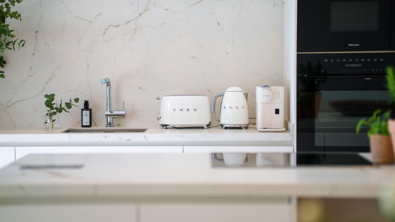 Close-up of a kitchen counter with white Smeg appliances, a sink, and marble backsplash.