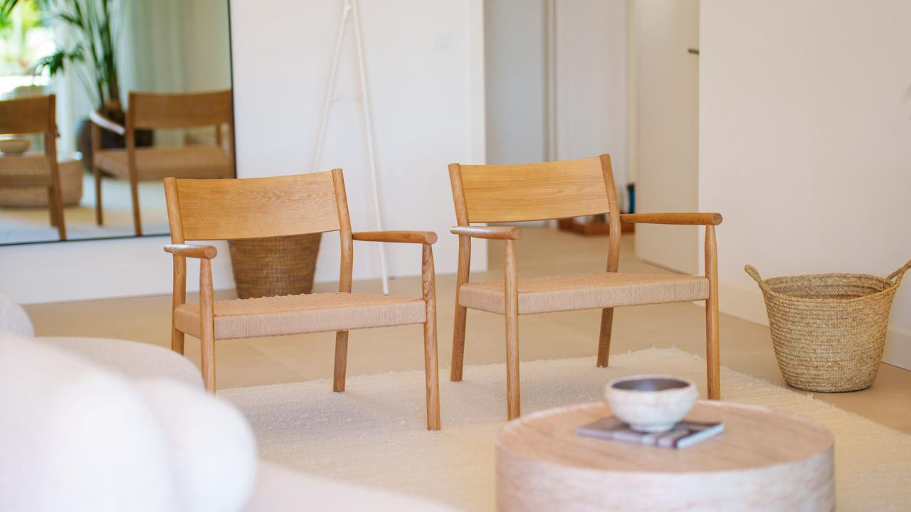 Two wooden armchairs with woven seats on a white rug, with a round coffee table in the foreground.