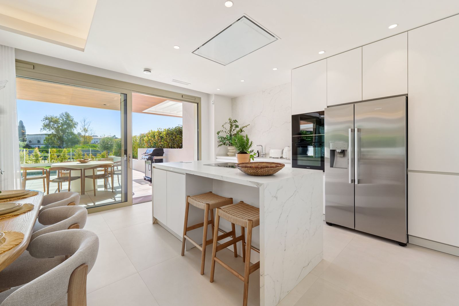 Modern kitchen with large island, stainless steel refrigerator, and glass doors opening to an outdoor patio.