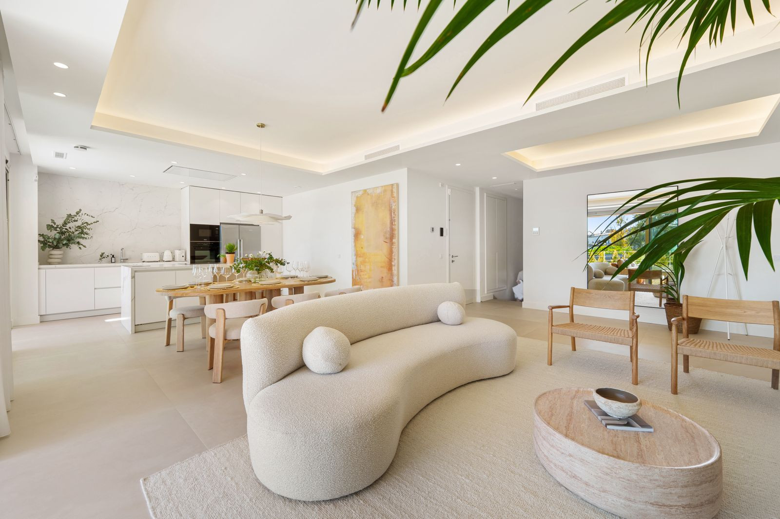 Open concept living room and kitchen with a curved white sofa, dining table, and light wood chairs.