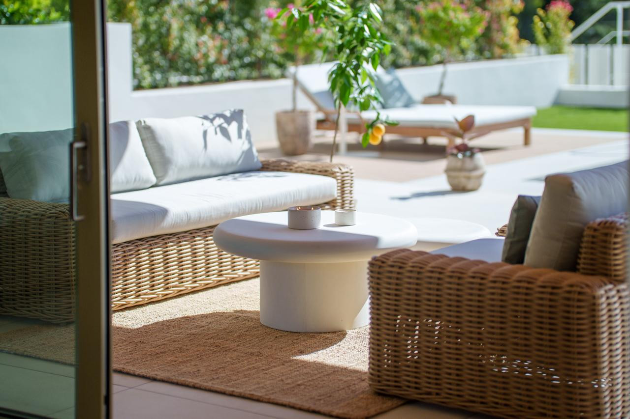 Close-up of outdoor wicker furniture and a coffee table, with a plant in the background.