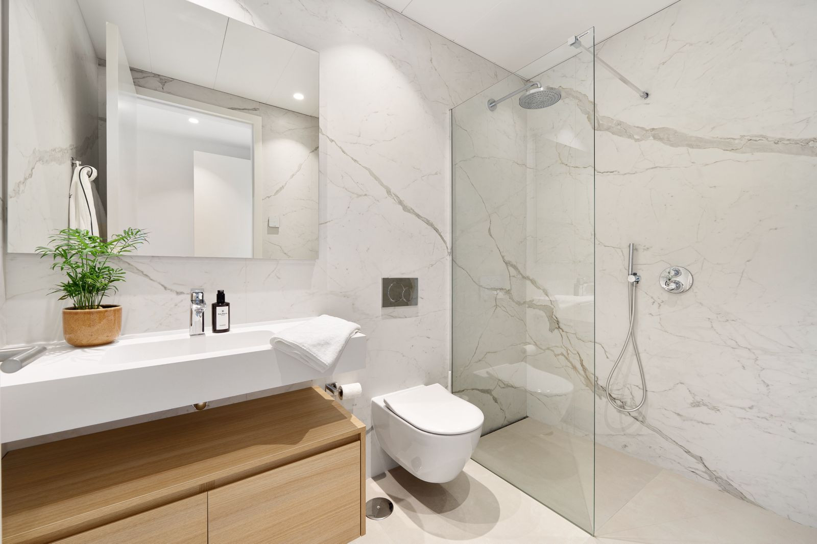 Modern bathroom with a walk-in shower, large white marble tiles, a floating vanity with a basin, and a wall-mounted toil