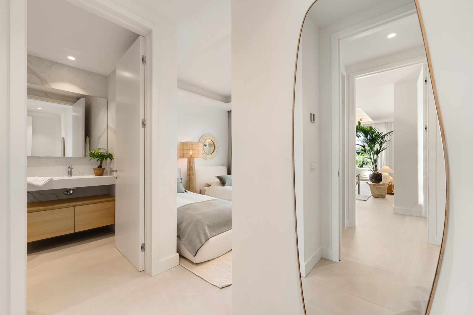 Hallway view showing a bathroom with vanity and a bedroom with twin beds and decorative mirror.