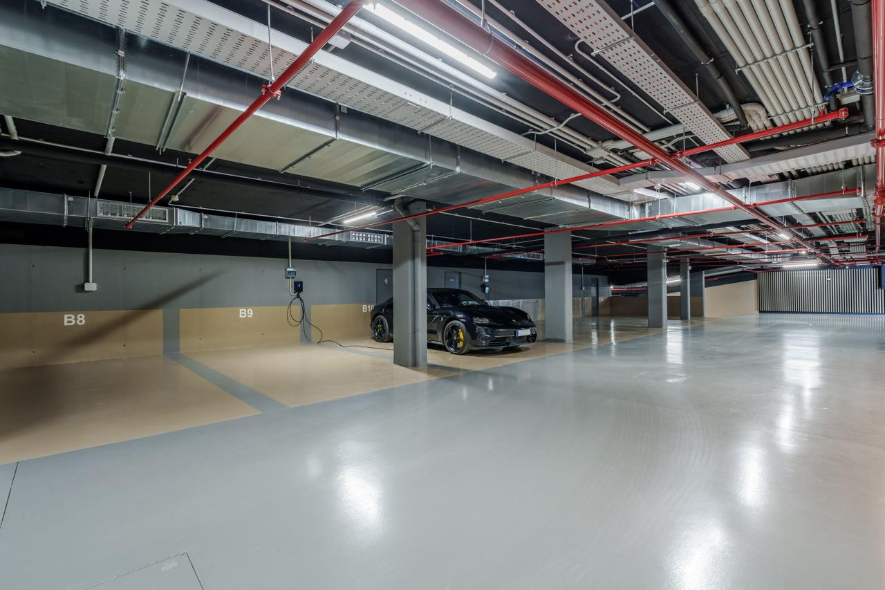 Underground parking garage with a dark luxury car charging, painted columns, and exposed utilities on the ceiling.