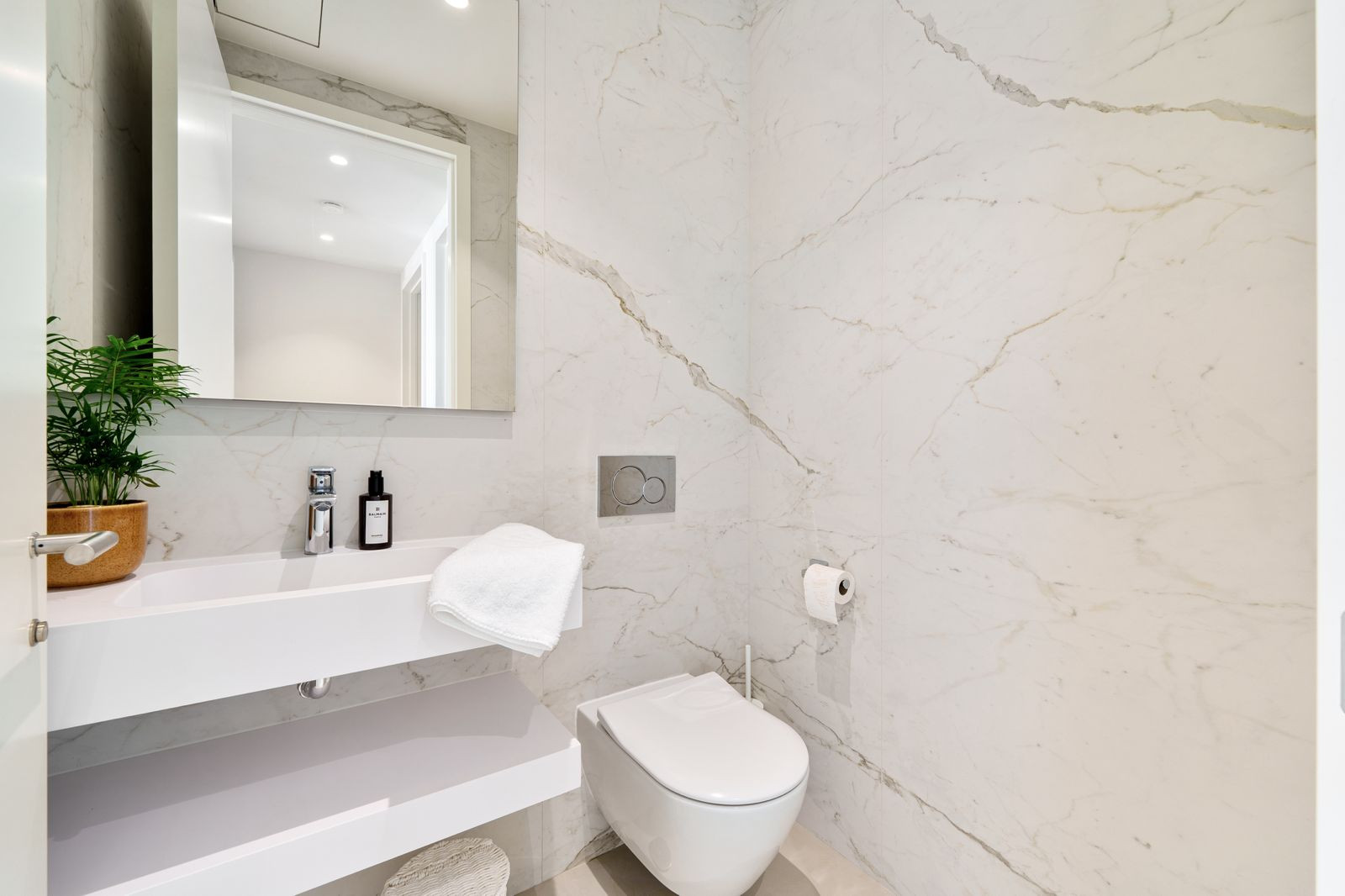 Modern bathroom with white marble walls, a floating vanity, and a wall-mounted toilet.