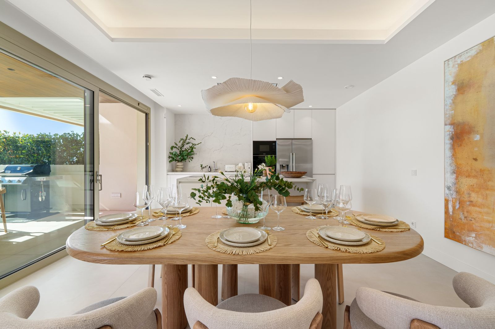 Dining area with a large oval wooden table set for six, under a petal-shaped pendant light.