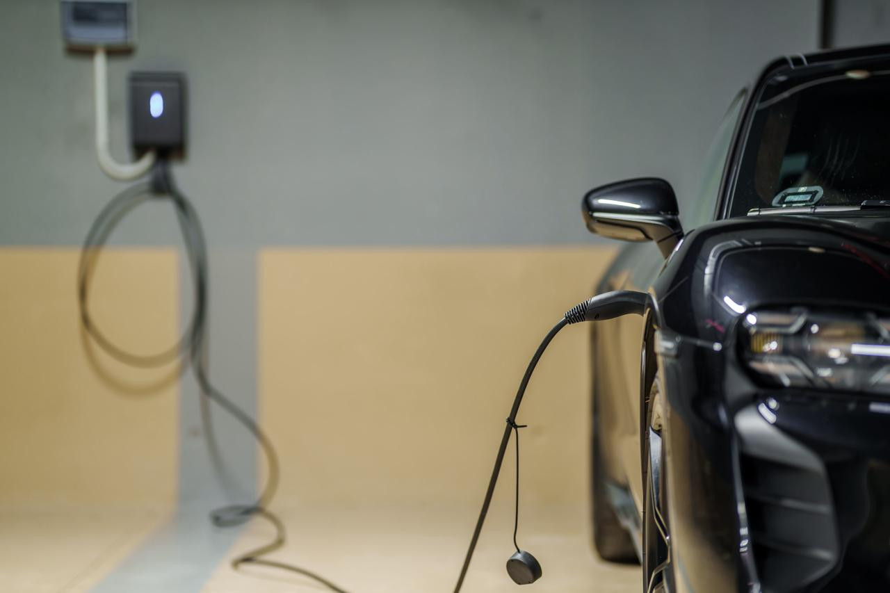 Close-up of a black electric car charging in a garage, with the charger mounted on the wall.