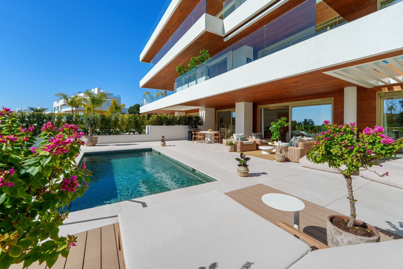 Outdoor patio with rectangular swimming pool, lounge area, and modern building exterior under a blue sky.