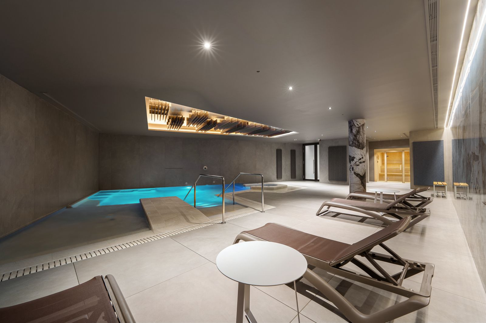 Indoor swimming pool area with lounge chairs, recessed lighting, and a unique illuminated ceiling feature.