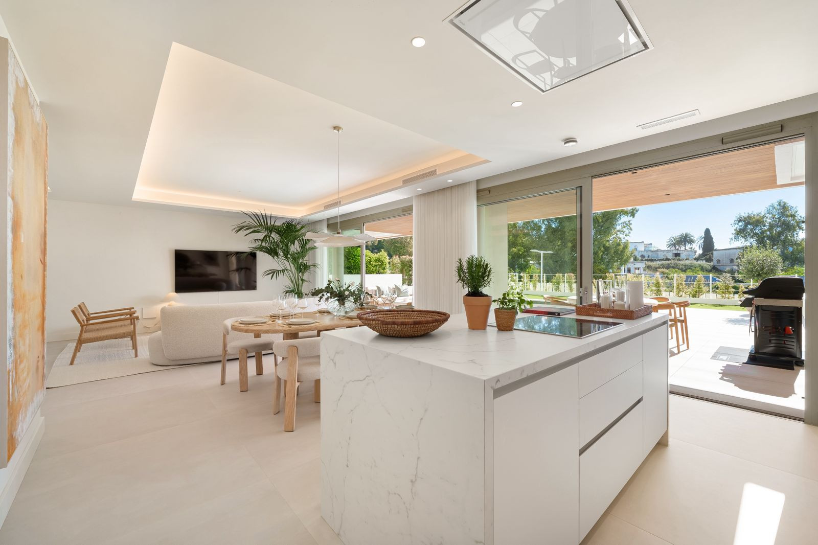 Open-plan living space with kitchen island, dining table, and sofa, leading to an outdoor area.