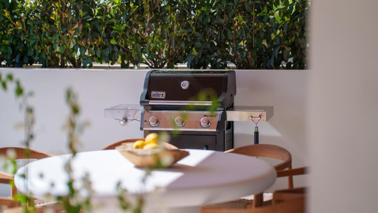 Close-up of a black Weber grill on a white patio next to a white table with a bowl of lemons.