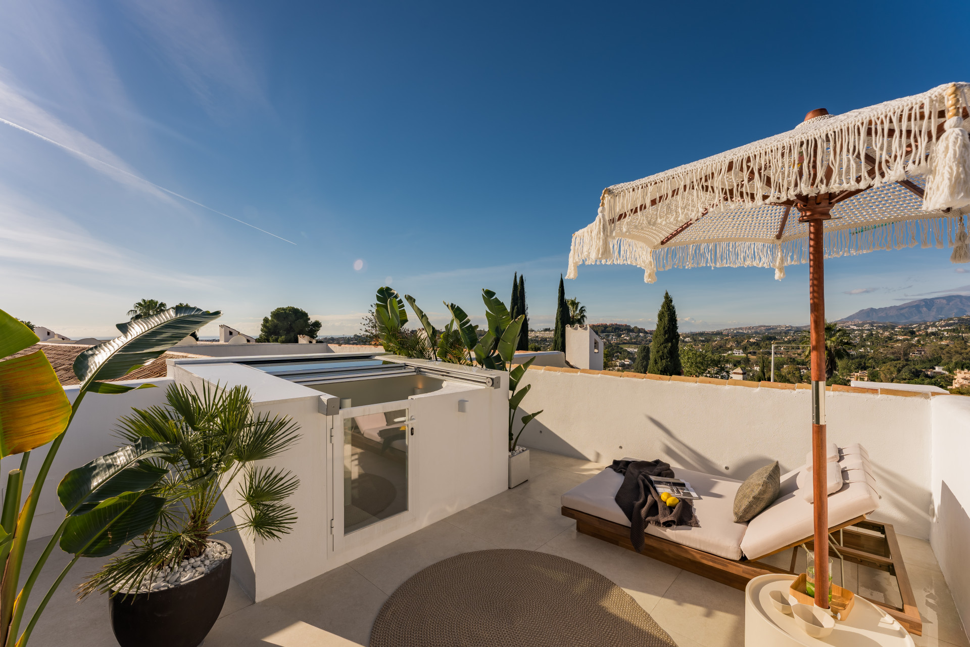 Rooftop terrace with a daybed, decorative umbrella, plants, and scenic distant views.