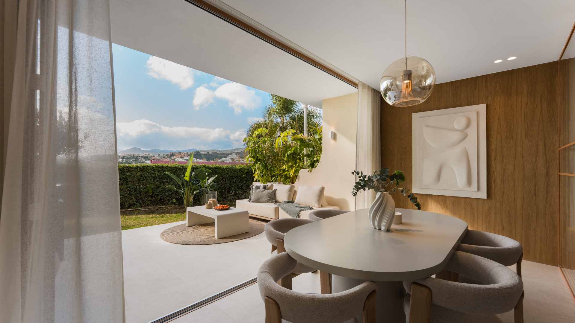 Dining room with oval table and chairs, connected to an outdoor patio with sofa and garden views.