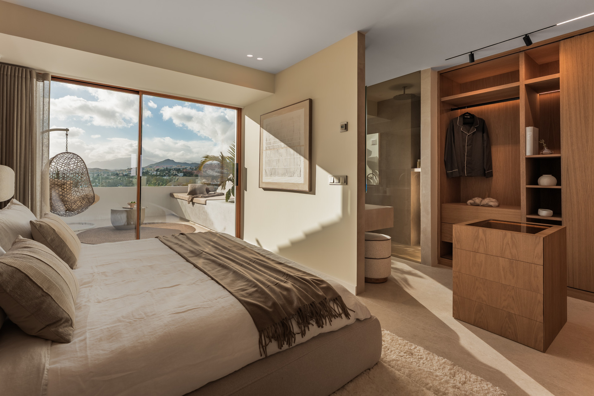 Bedroom with a large bed, walk-in closet, and glass doors opening to a terrace with a hanging chair.