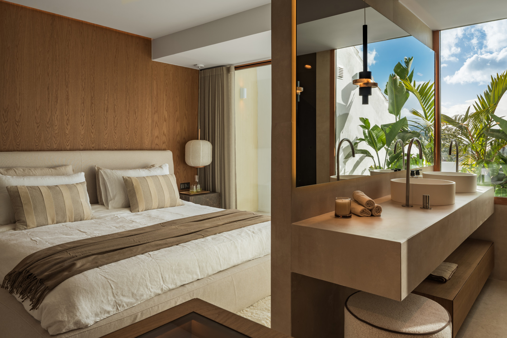 Bedroom with a large bed and an open-concept bathroom featuring a dual vanity and large window.