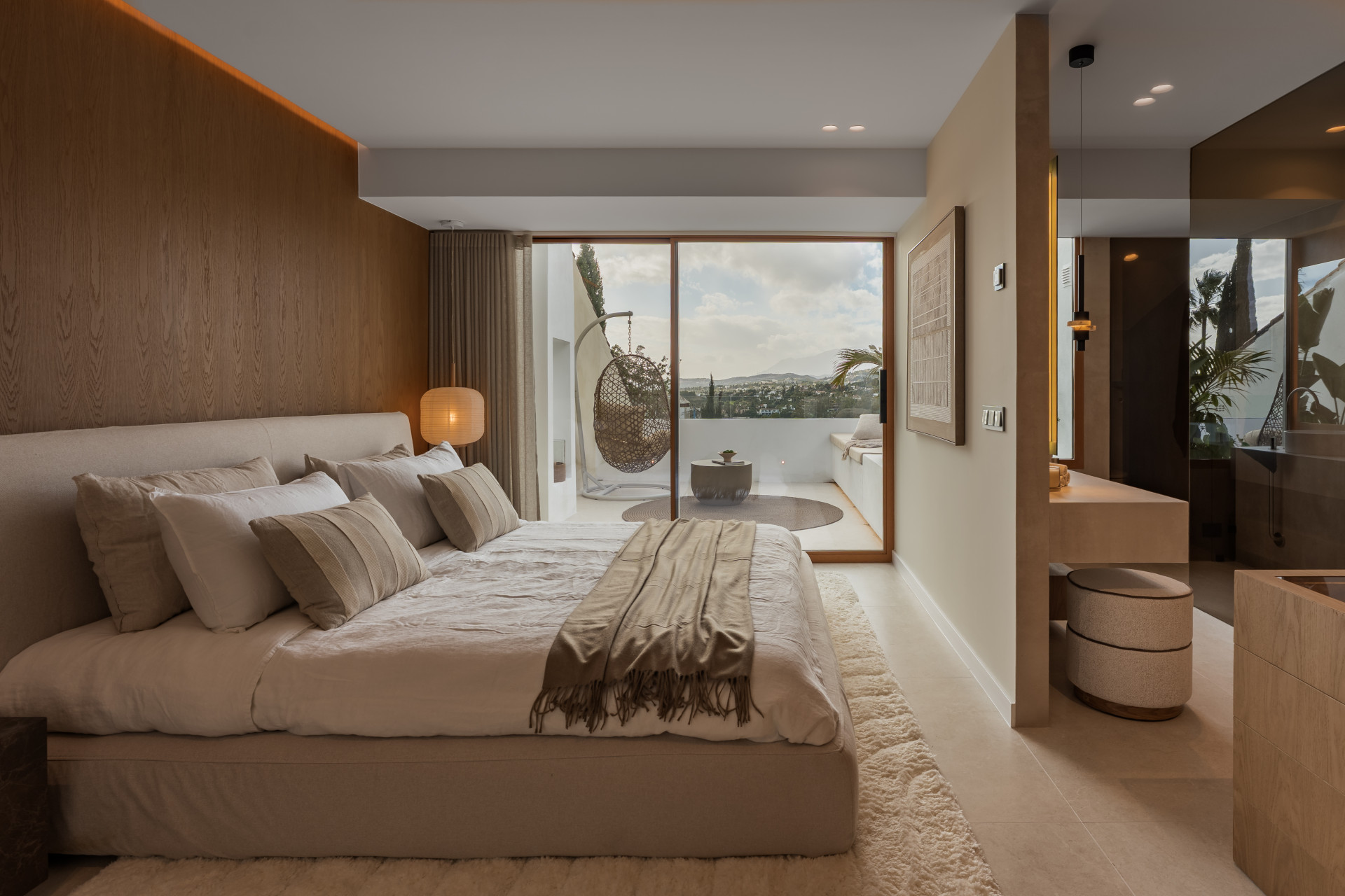 Bedroom with a large bed, wooden wall paneling, and an outdoor balcony with a hanging chair and views.