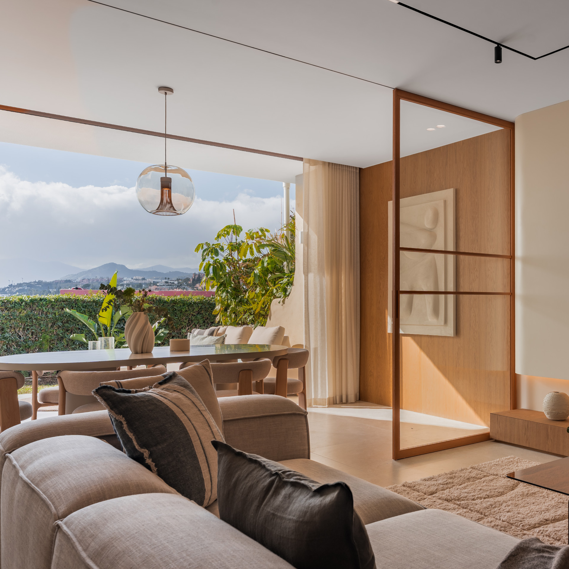 Sofa in foreground facing an outdoor dining area with a glass table, showing distant mountains.