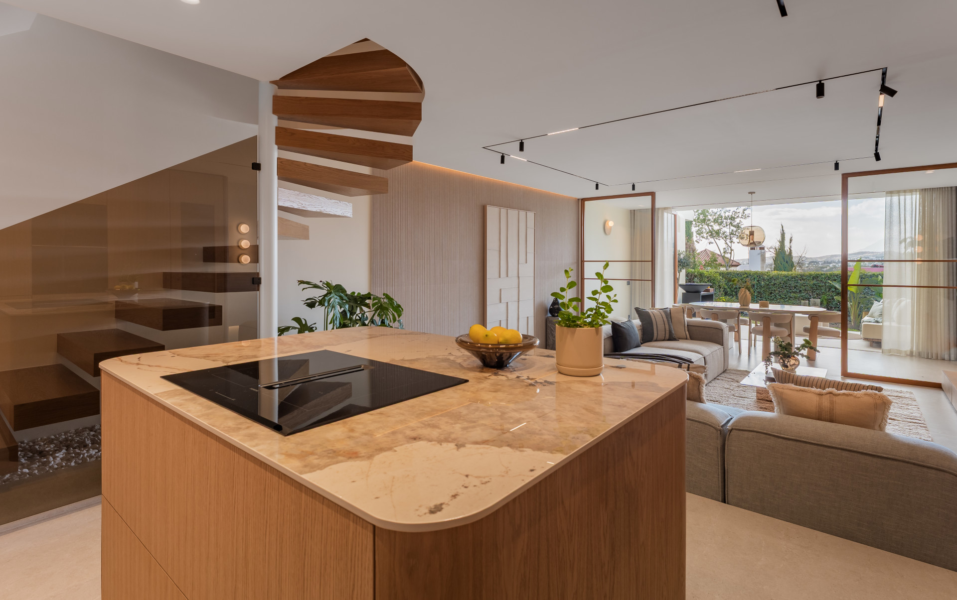 Kitchen island with cooktop and a view of the spiral staircase and living dining area leading to a patio.