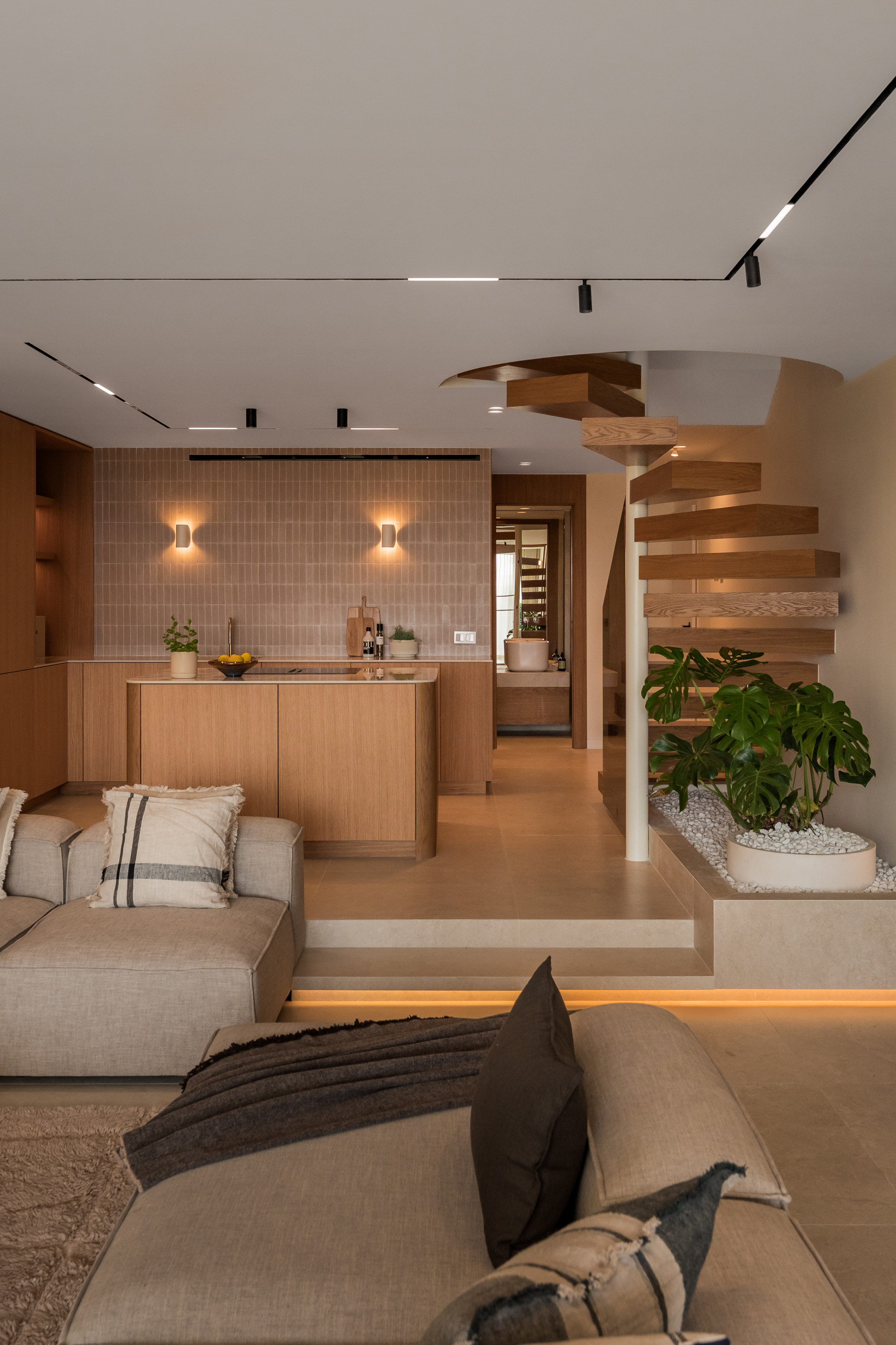 Open living area with a kitchen island, beige sectional sofa, and a spiral wooden staircase leading up.