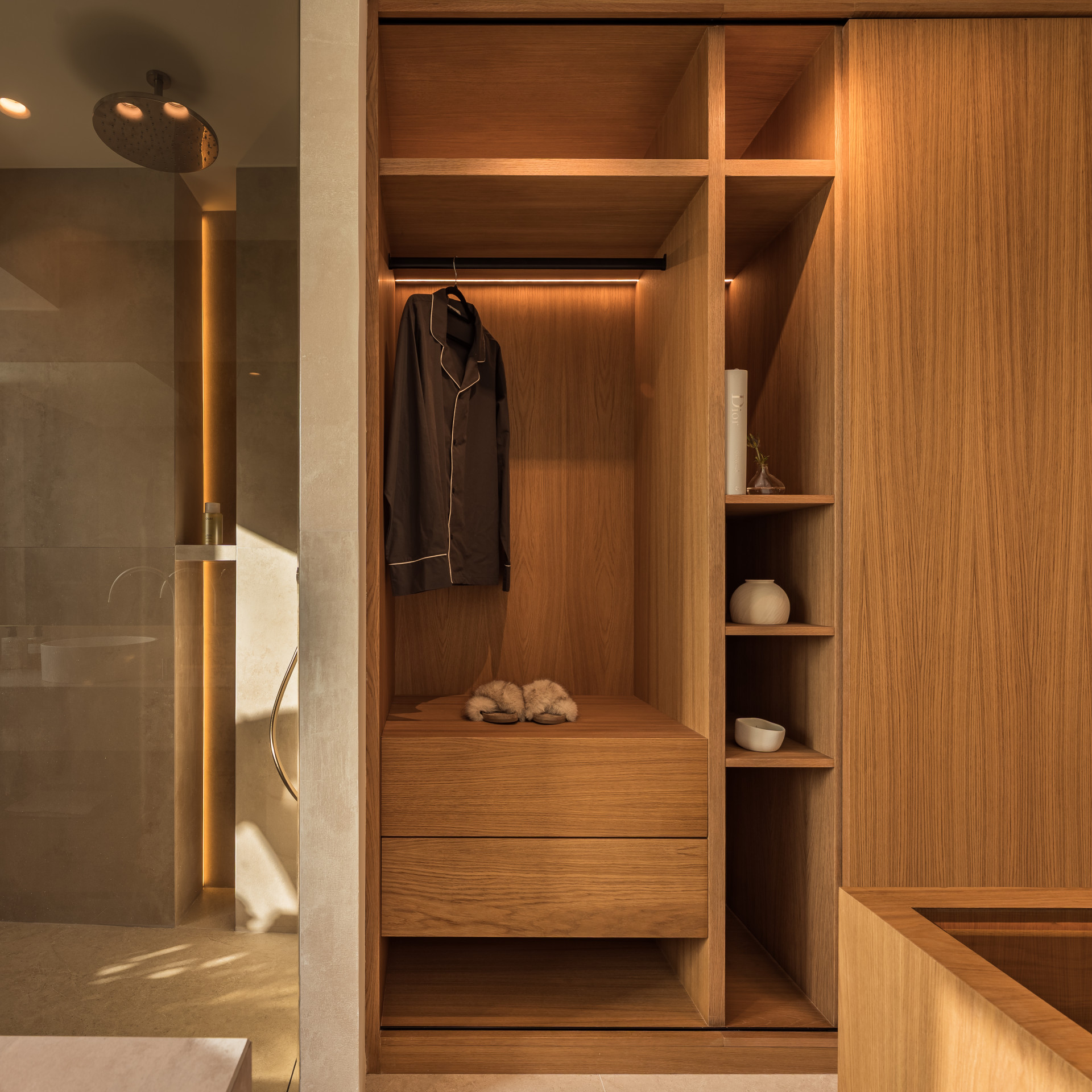 Open closet with brown pajamas next to a walk-in shower with gold fixtures.