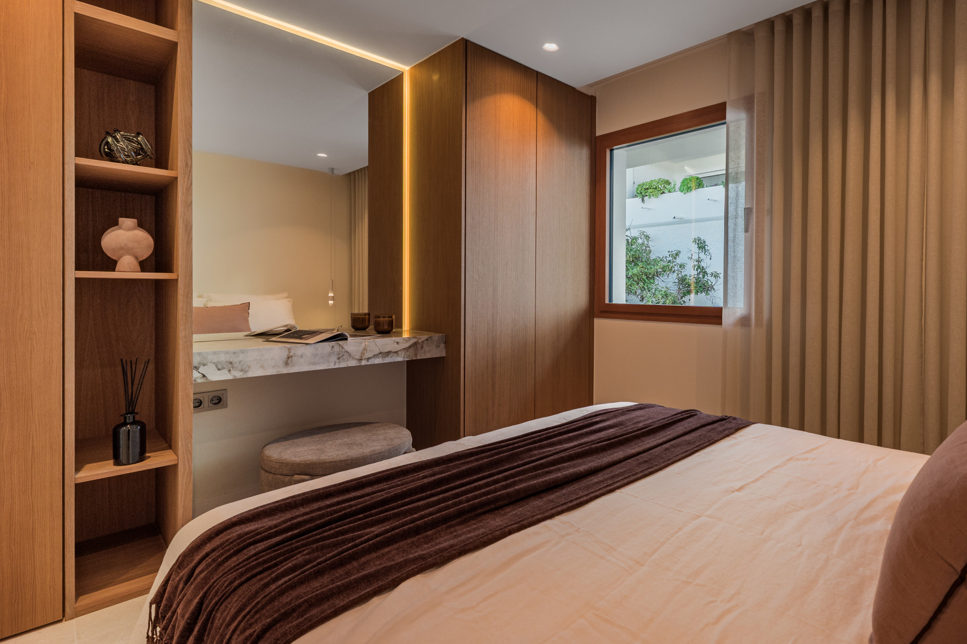 Bedroom with a large bed, built-in wooden closet, a vanity desk, and a window with a green view.