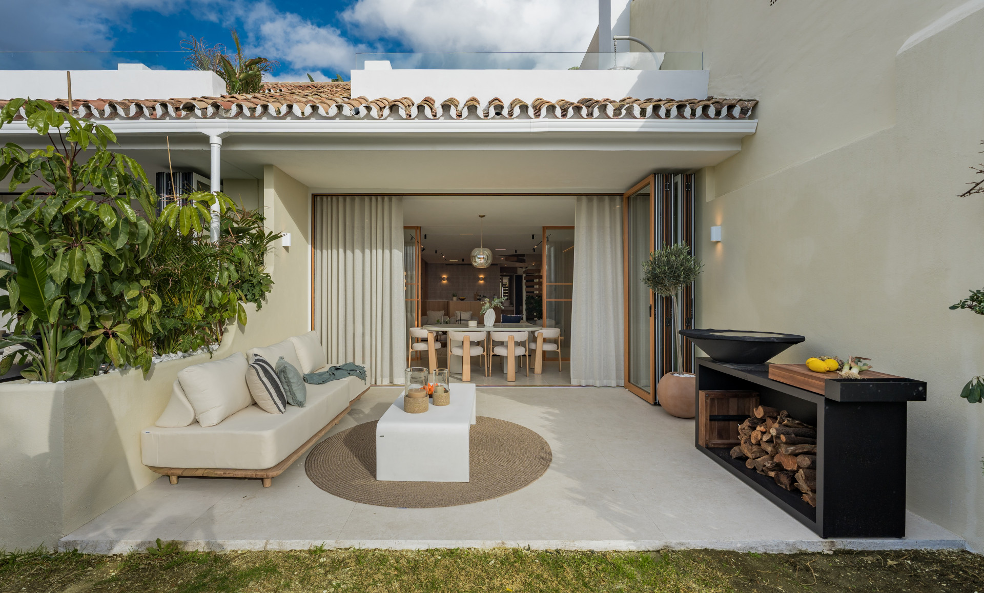 Outdoor patio with lounge sofa, coffee table, BBQ, and dining room visible through glass doors.