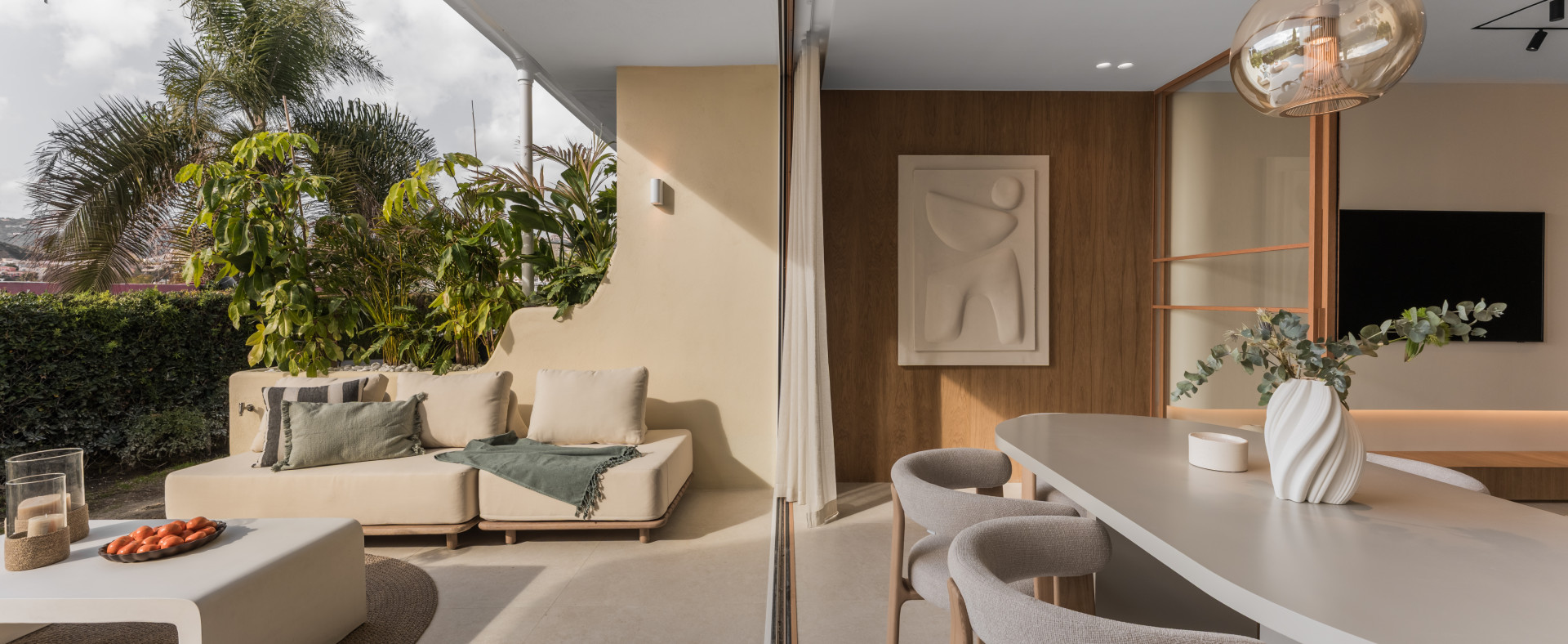 Outdoor lounge sofa with cushions and throw blanket, beside an indoor dining area with a long table.