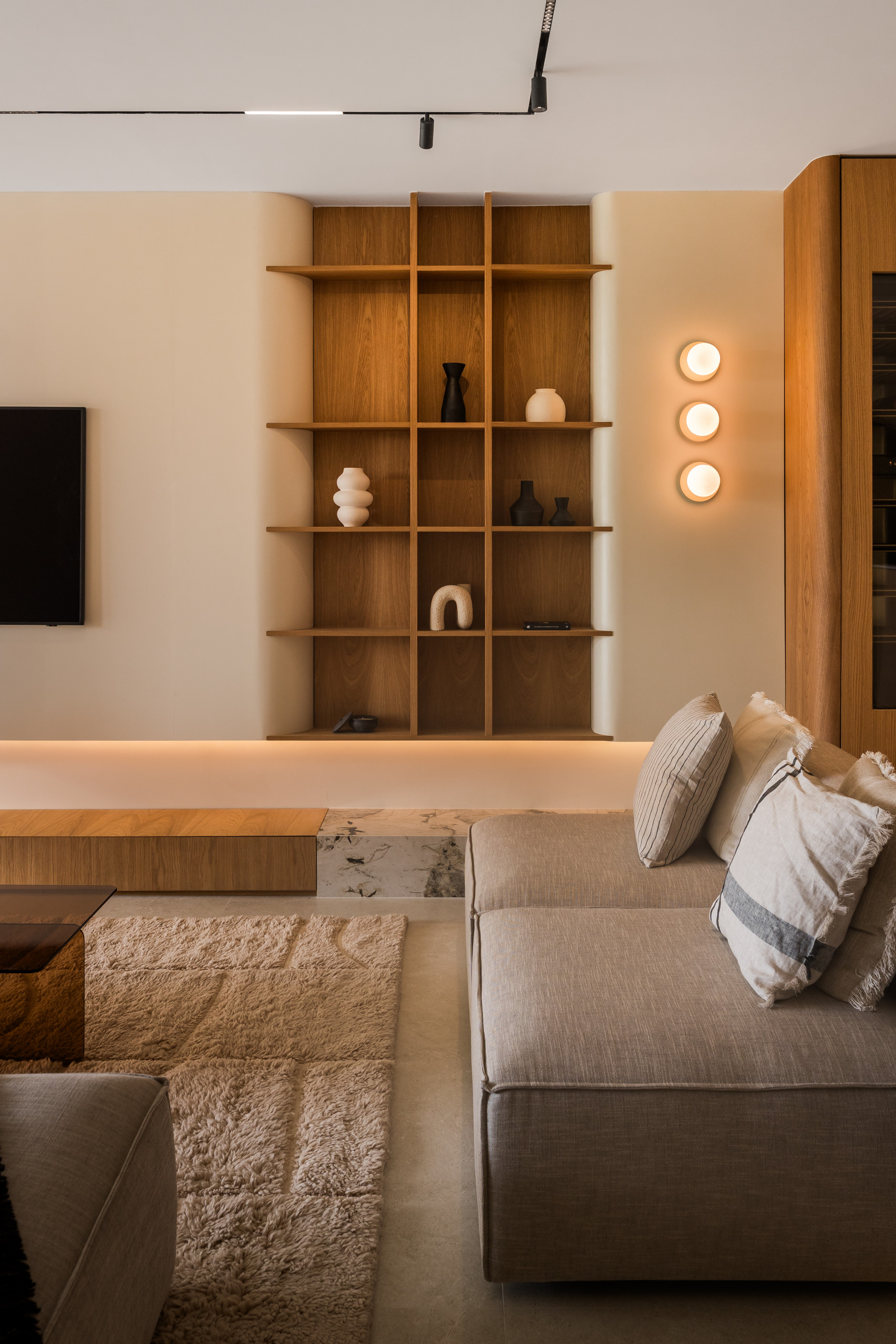 Living room with a large L-shaped sofa, rug, and built-in wooden shelving displaying decorative objects.