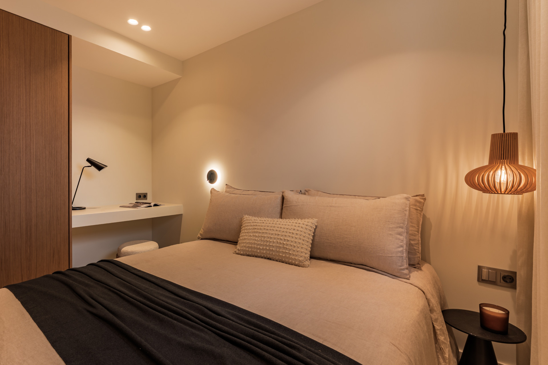 Bedroom with a large bed, overhead hanging light, desk, and bedside table.