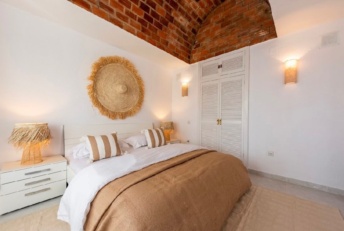 Bedroom featuring a bed with striped pillows, white nightstands, and a vaulted brick ceiling.