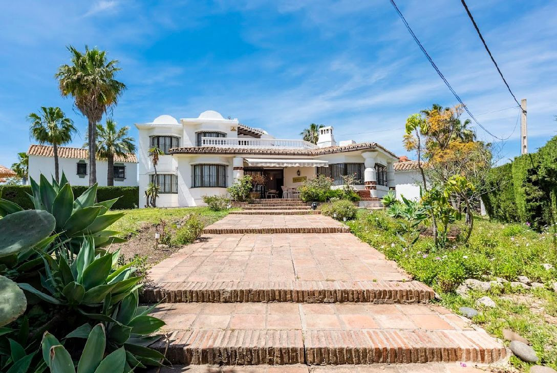 Front exterior of a white villa with a terracotta tile path leading to the entrance, flanked by agave plants.