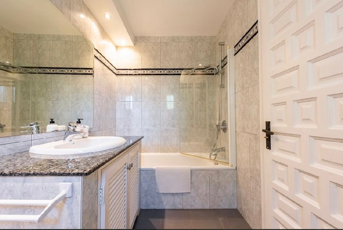 Bathroom with tiled walls, corner bathtub with shower, white vanity with granite top and sink.