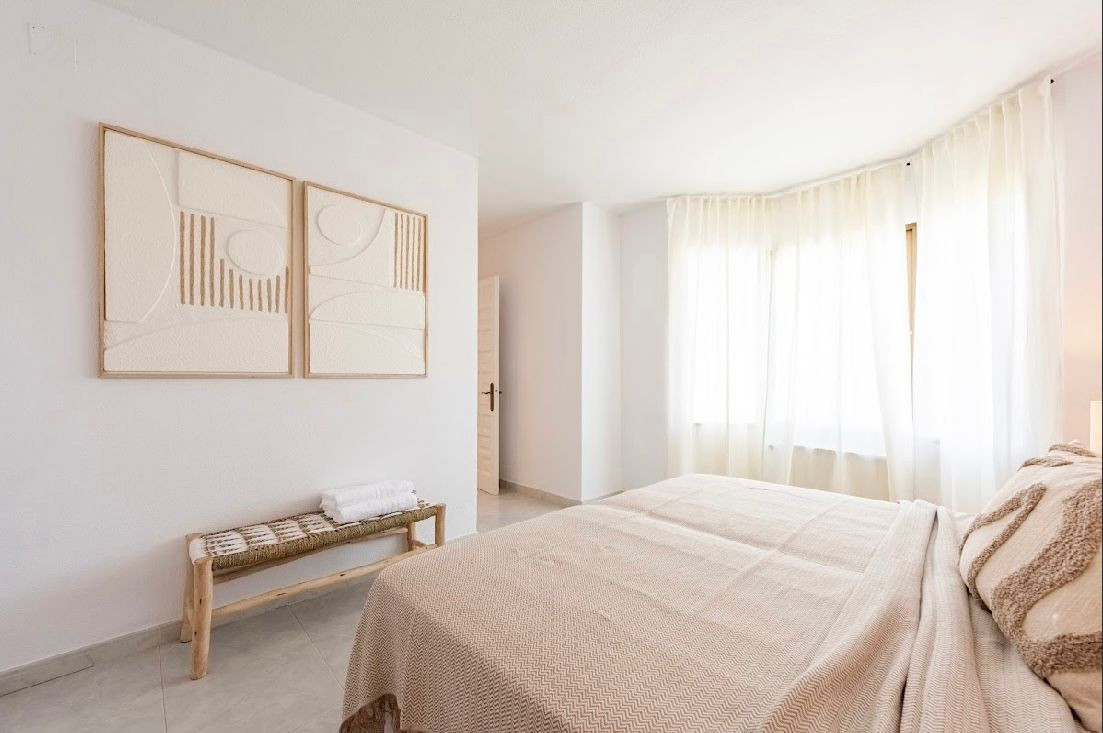 Bright bedroom with two beds, large window with sheer curtains, and two framed abstract artworks.
