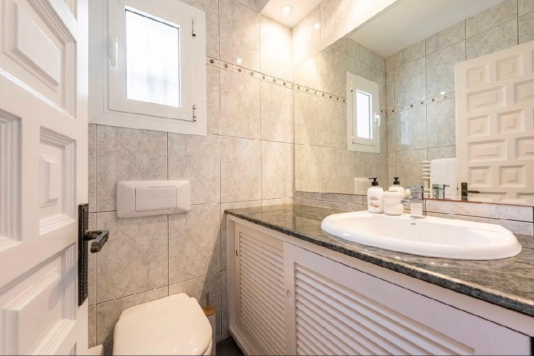 Bathroom with light-tiled walls, a toilet, vanity with dark countertop, and a mirror.