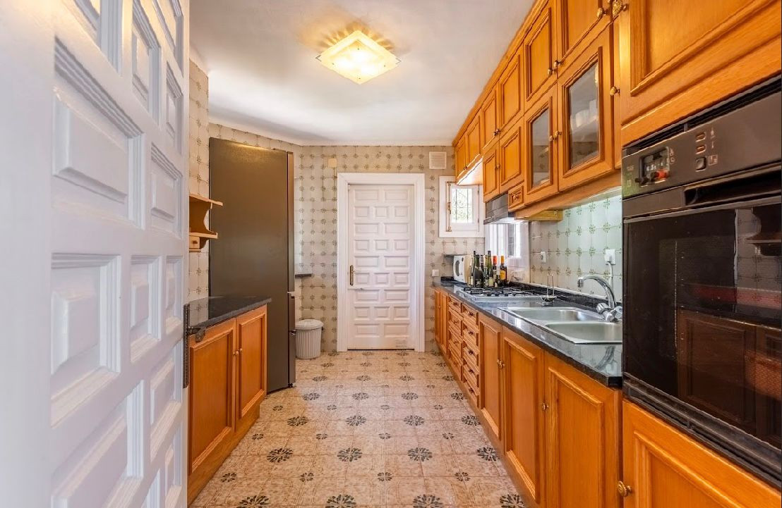 Narrow galley kitchen featuring wooden cabinets, black countertops, and patterned floor tiles.