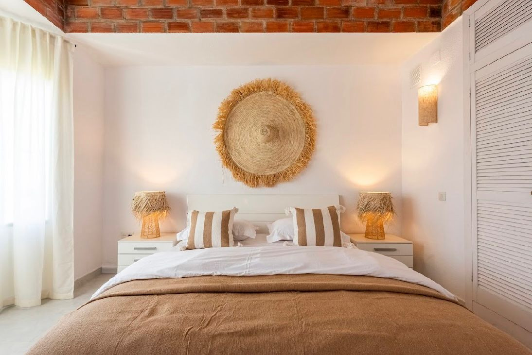 Bedroom with a large bed, two nightstands, a straw wall decoration, and an exposed brick ceiling.