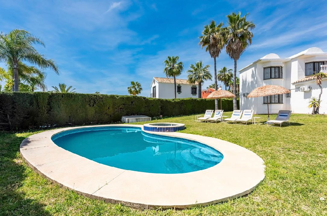 Curved swimming pool with steps, surrounded by green grass, sun loungers, and a white villa exterior.