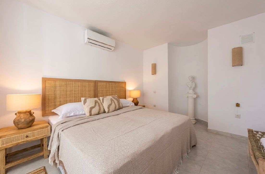 Bedroom with a large bed, woven headboard, two nightstands, and a white bust on a pedestal.