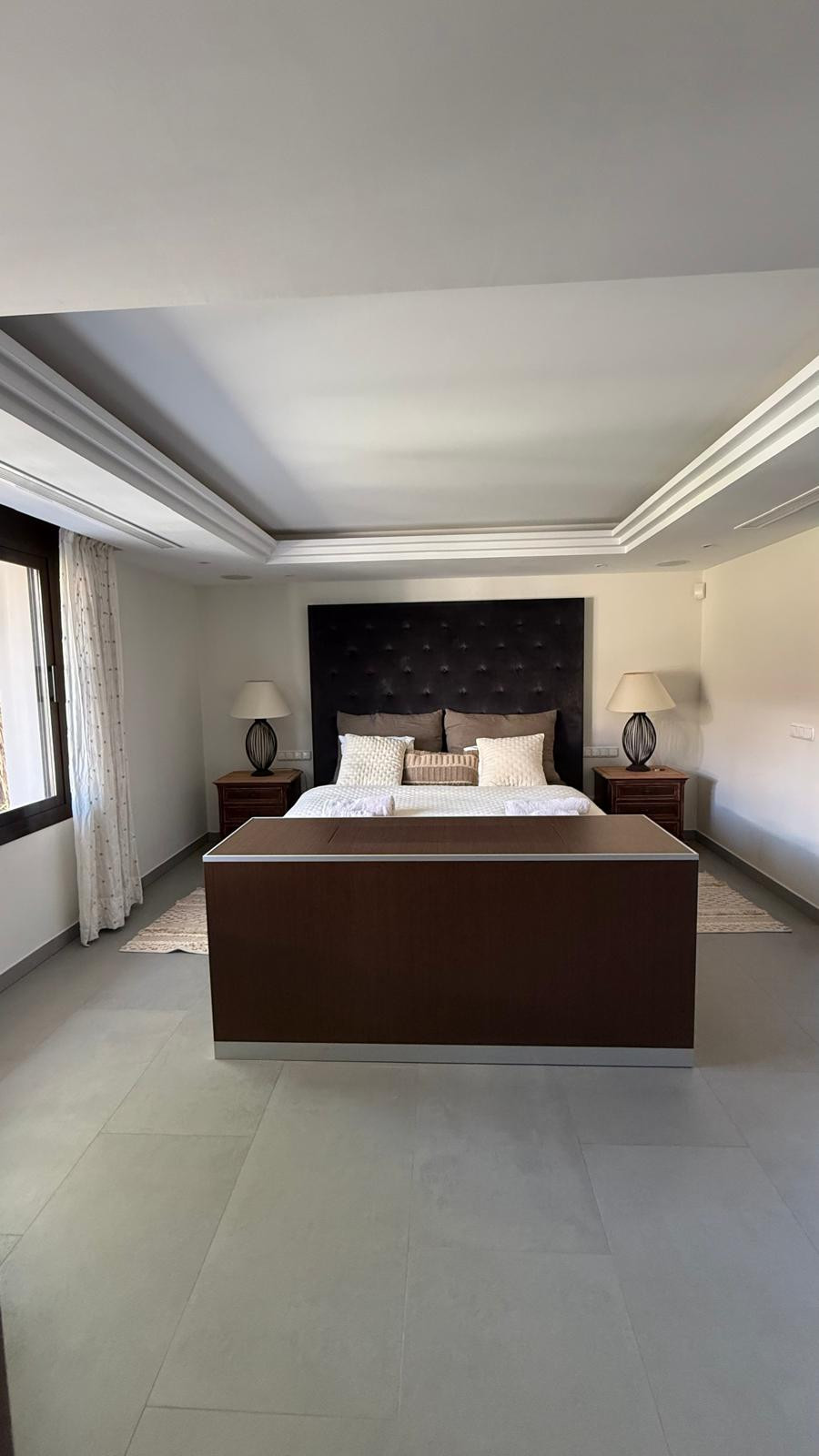 Spacious bedroom showcasing a tufted headboard, bedside lamps, and ample storage.