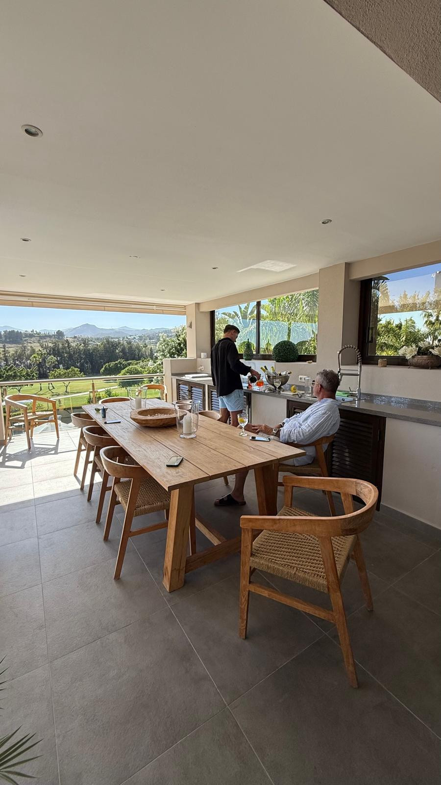 Spacious kitchen-dining area with a wooden table and outdoor view, featuring a grill and modern appliances.