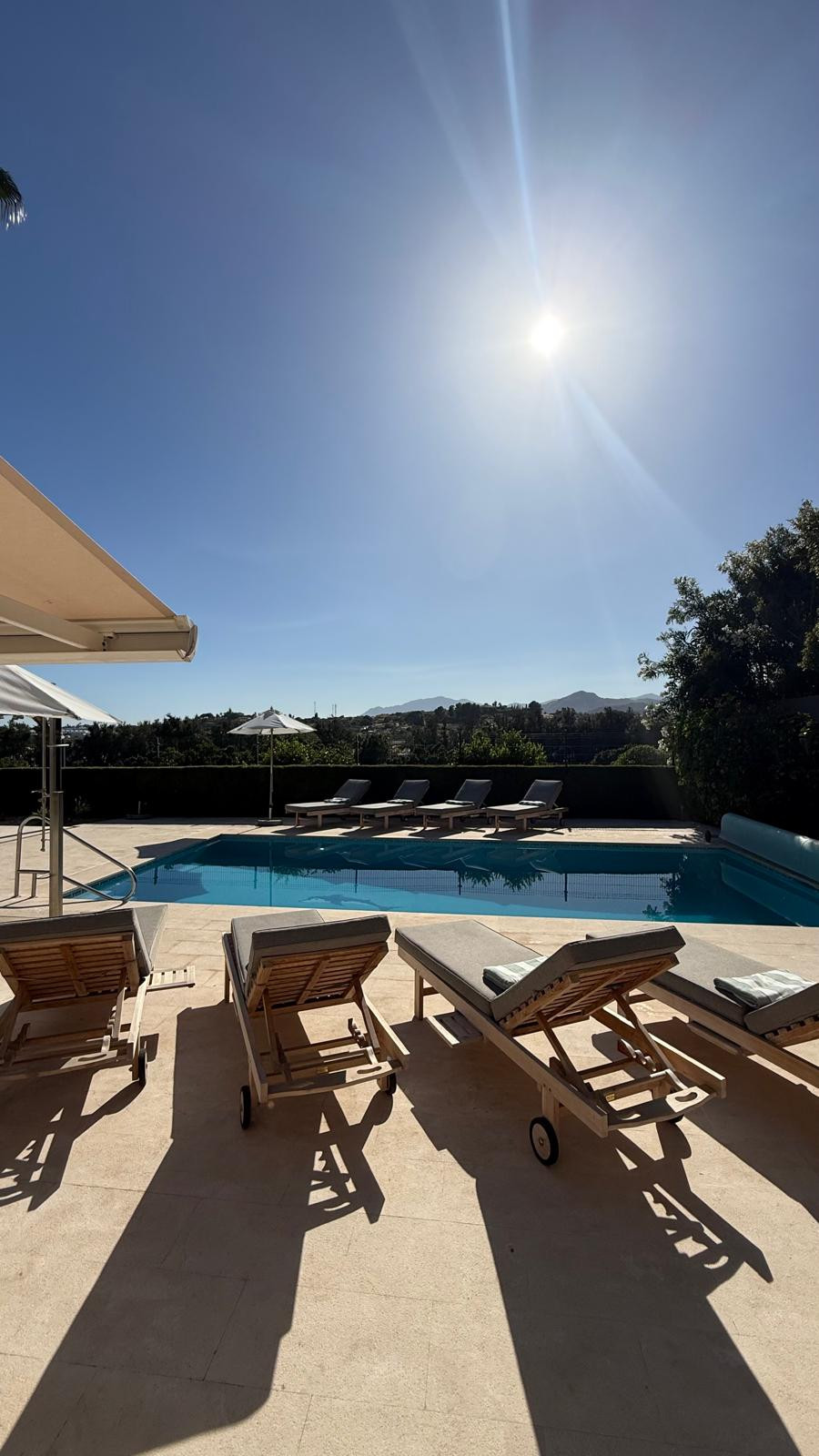 Outdoor pool area with sun loungers and umbrellas under a clear sky.